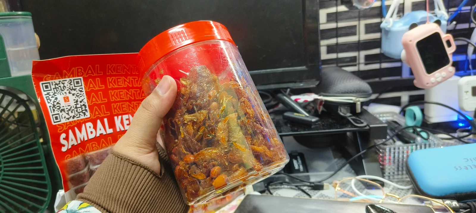 Sambal kentang goreng dalam balang dipegang tangan dengan latar meja kerja rumah